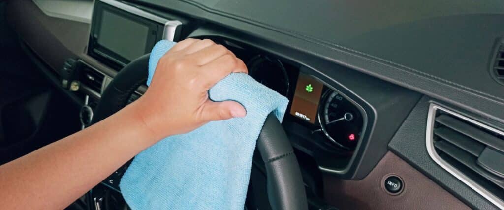 Main nettoyant le volant et le tableau de bord d'une voiture avec une microfibre bleue