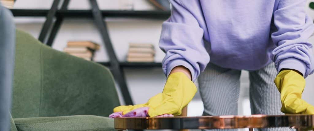 Mains gantées faisant la poussière sur une table basse du salon